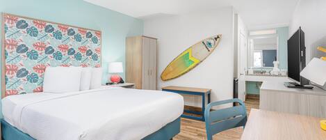 Habitación de hotel con cama, escritorio, silla, armario y una tabla de surf colgada en la pared.
