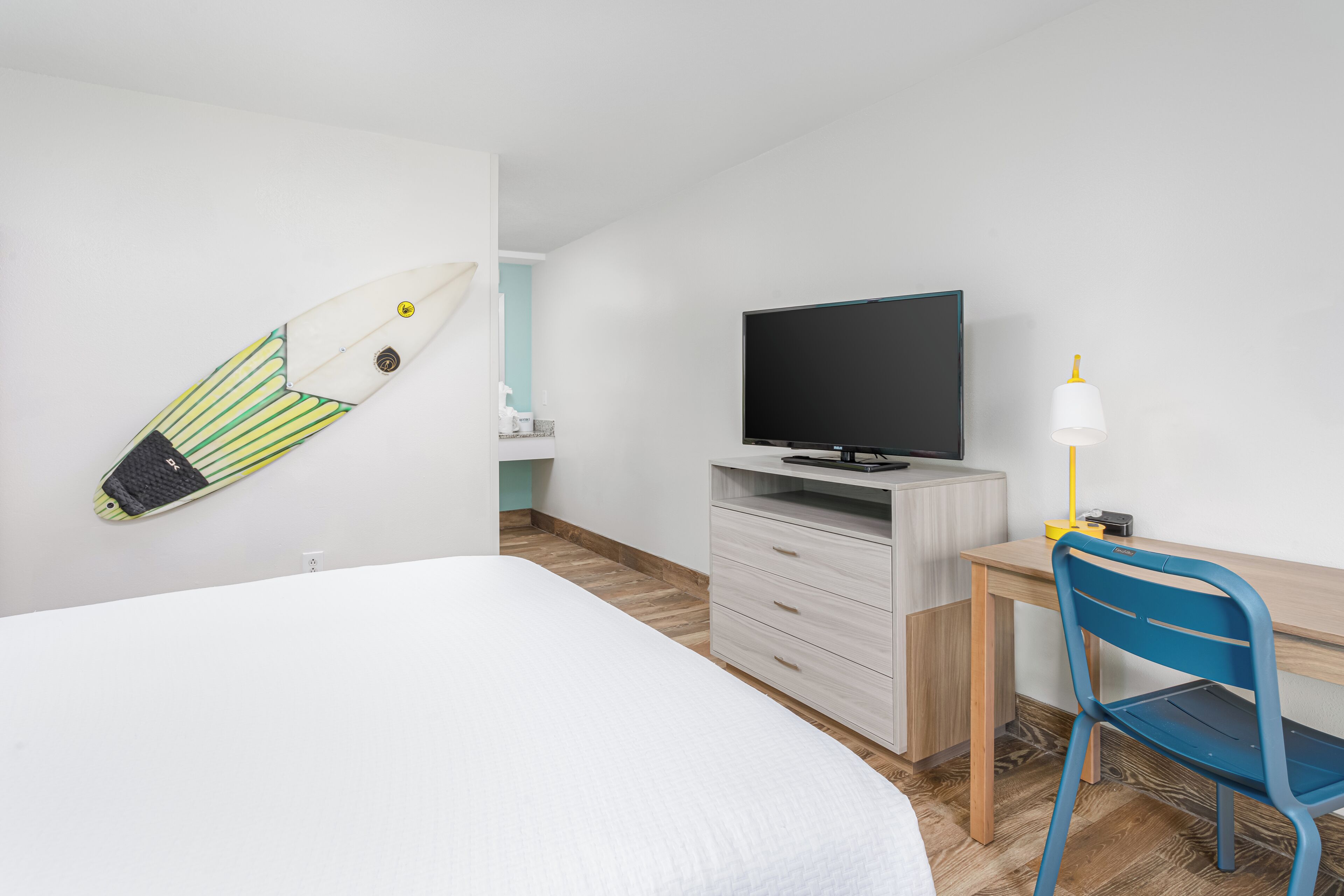 Une chambre d’hôtel avec un lit, un bureau et une chaise, une télévision et une planche de surf accrochée au mur.