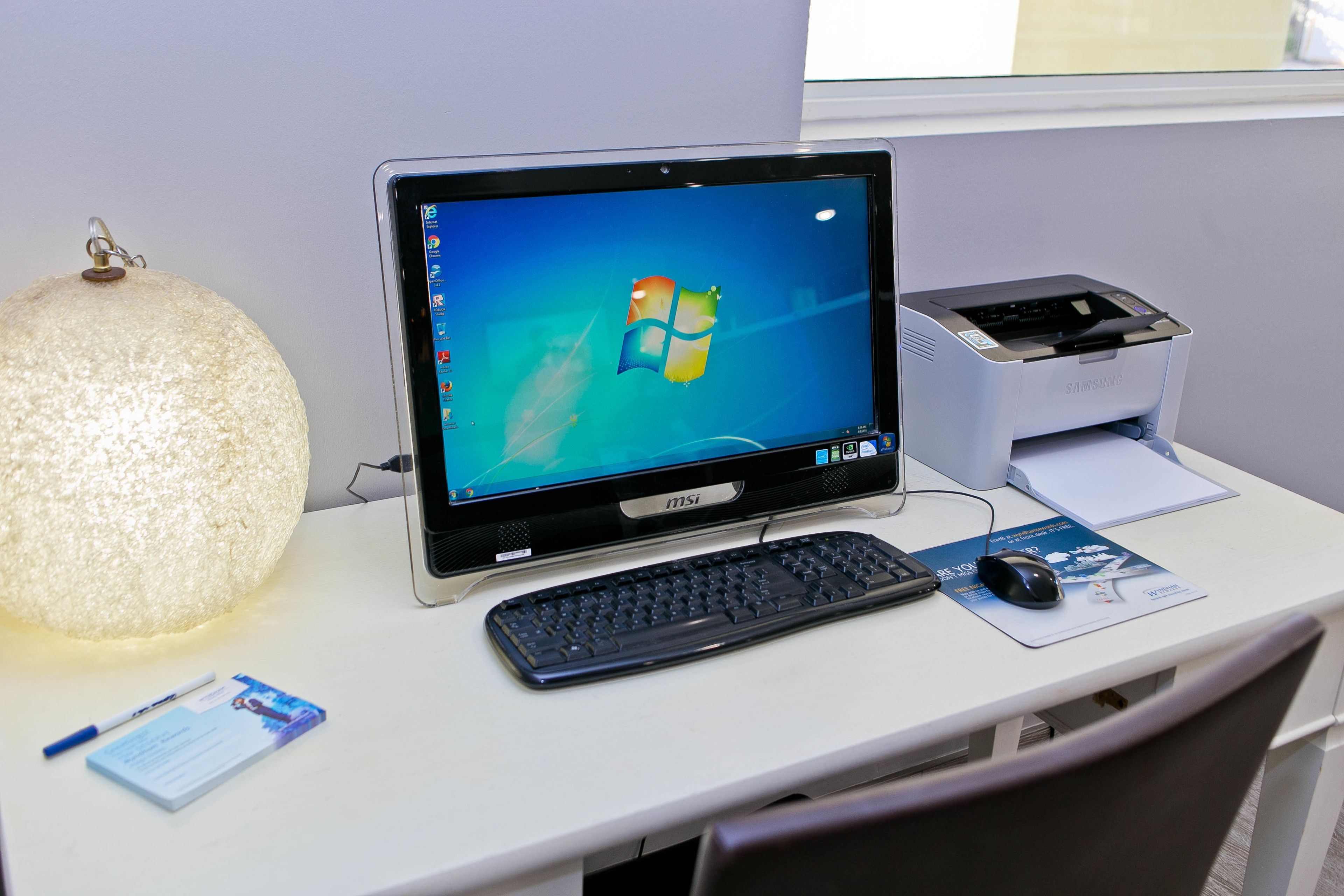 Un escritorio con una computadora de escritorio, un teclado, un ratón, una lámpara y algunos documentos.