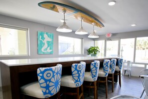 Un espace bar doté d’un plafond en forme de planche de surf, d’un comptoir blanc et de chaises à motifs bleus.