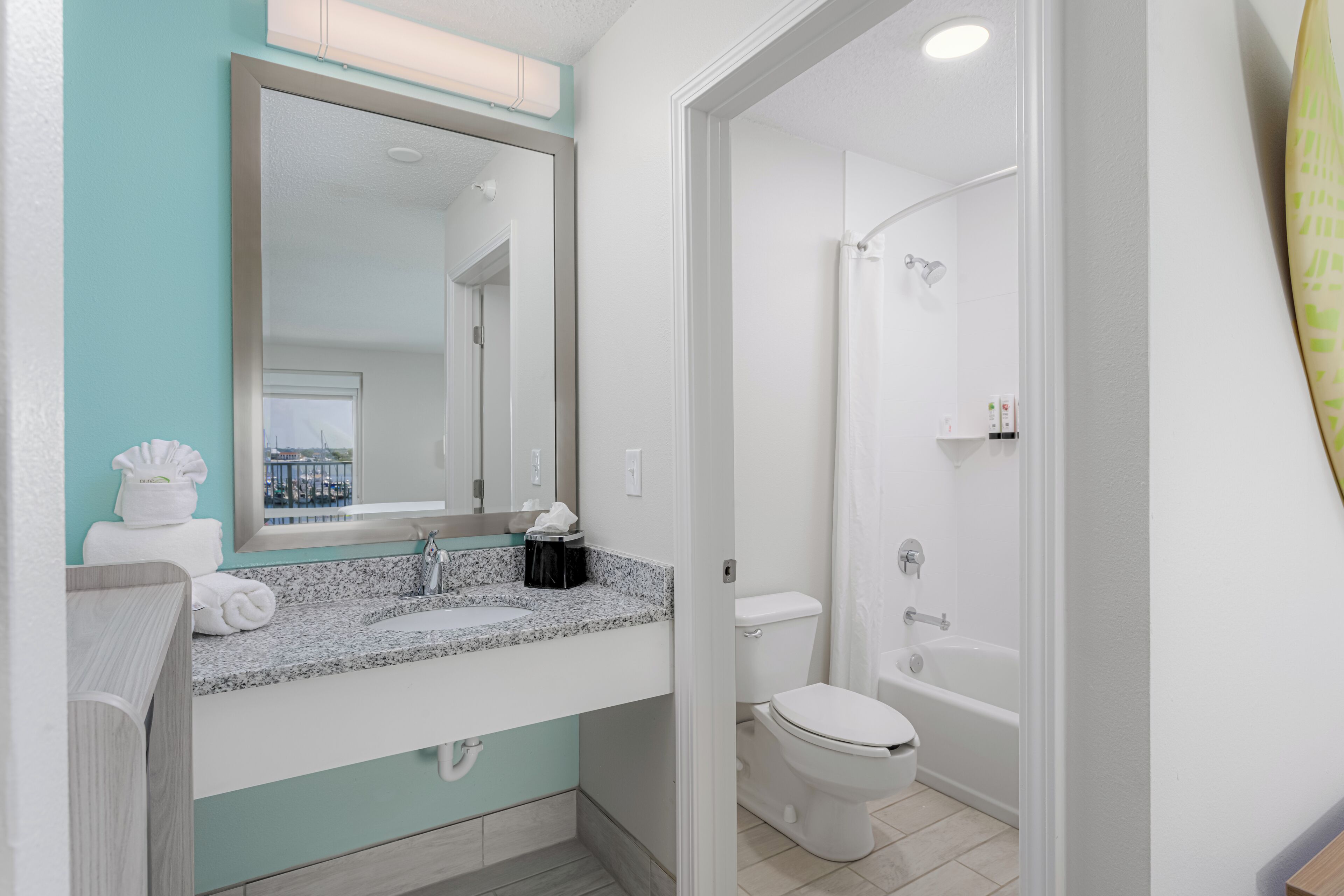 A modern bathroom with a granite countertop, a large mirror, a white toilet, and a bathtub.