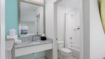 A modern bathroom with a granite countertop, a large mirror, a white toilet, and a bathtub.