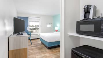 A hotel room with a bed, a television on a wooden cabinet, a microwave, and a coffee maker.