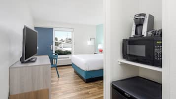 Habitación de hotel con cama, escritorio, televisión, microondas, cafetera y vista al exterior.