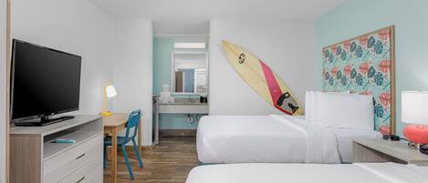 A hotel room with a TV, desk, chair, bed, and a surfboard on the wall.