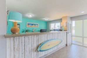 Un espace d’accueil avec un comptoir en bois, une planche de surf et un tableau accroché au mur.
