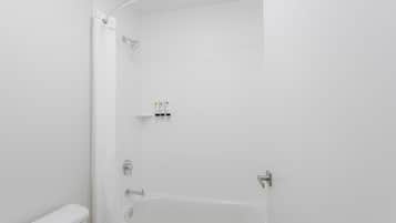 A modern bathroom with a white bathtub, a shower, and a toilet.