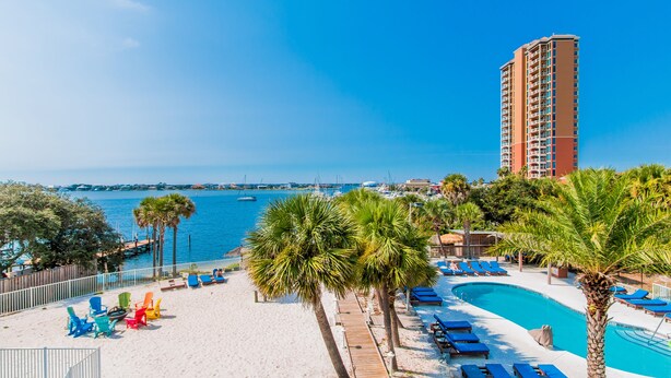 Un resort con piscina, sillas de playa, palmeras y vistas al mar y barcos.