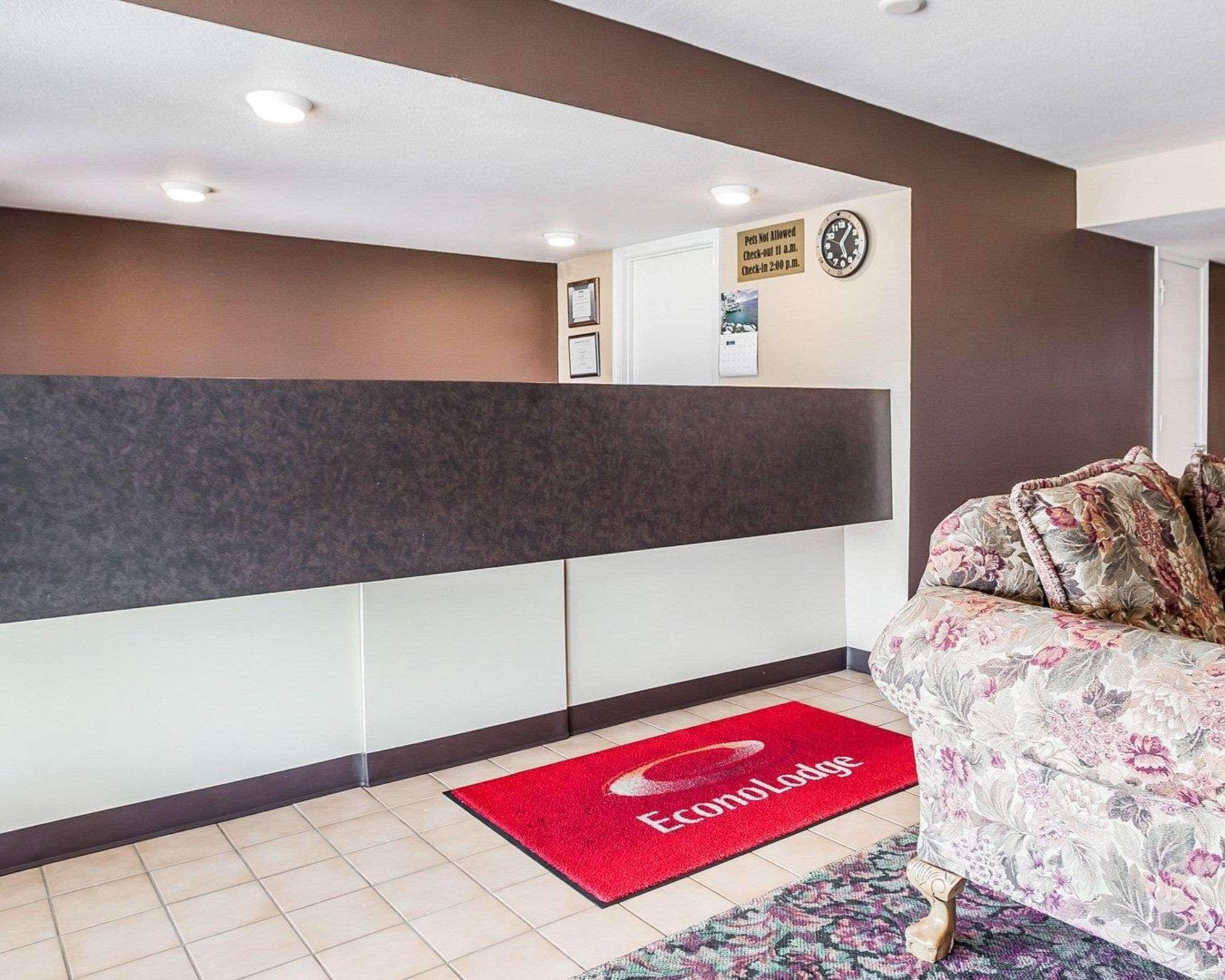 Área de recepção de hotel com balcão de check-in, um relógio e um aviso sobre a política para animais de estimação.