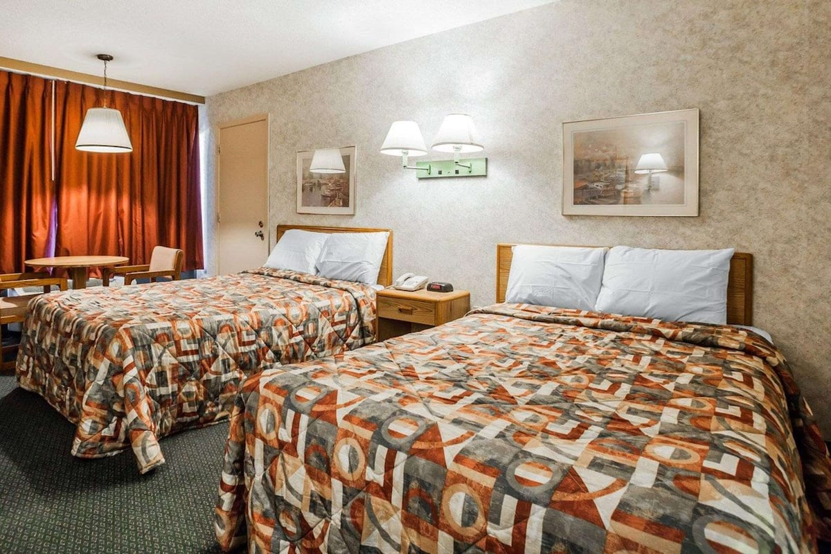 Hotellihuoneessa on kaksi sänkyä, työpöytä ja tuoli. Seinillä on seinävalaisimia ja kehystettyjä tauluja.