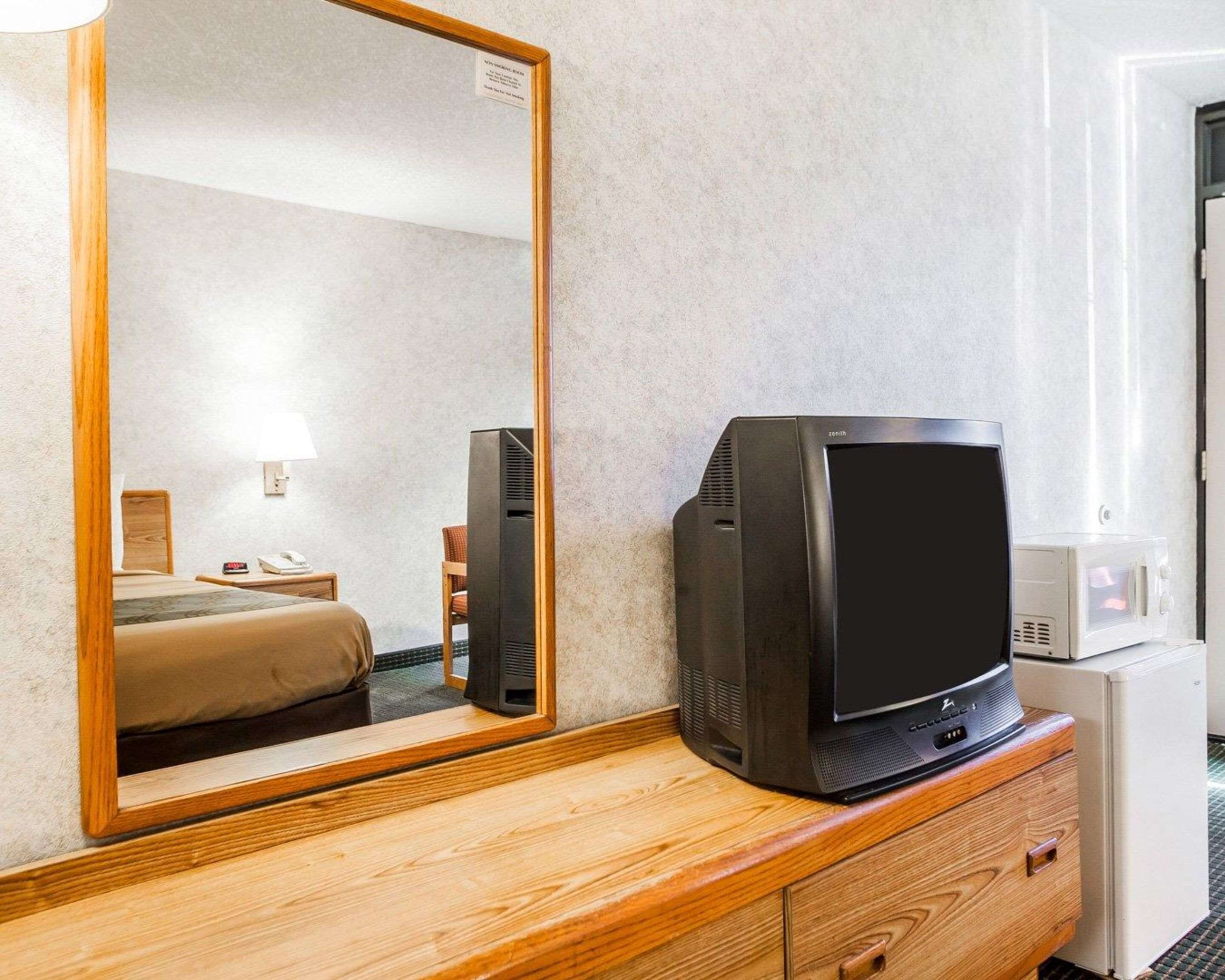 Quarto de hotel com cômoda de madeira, televisão, micro-ondas e uma cama.
