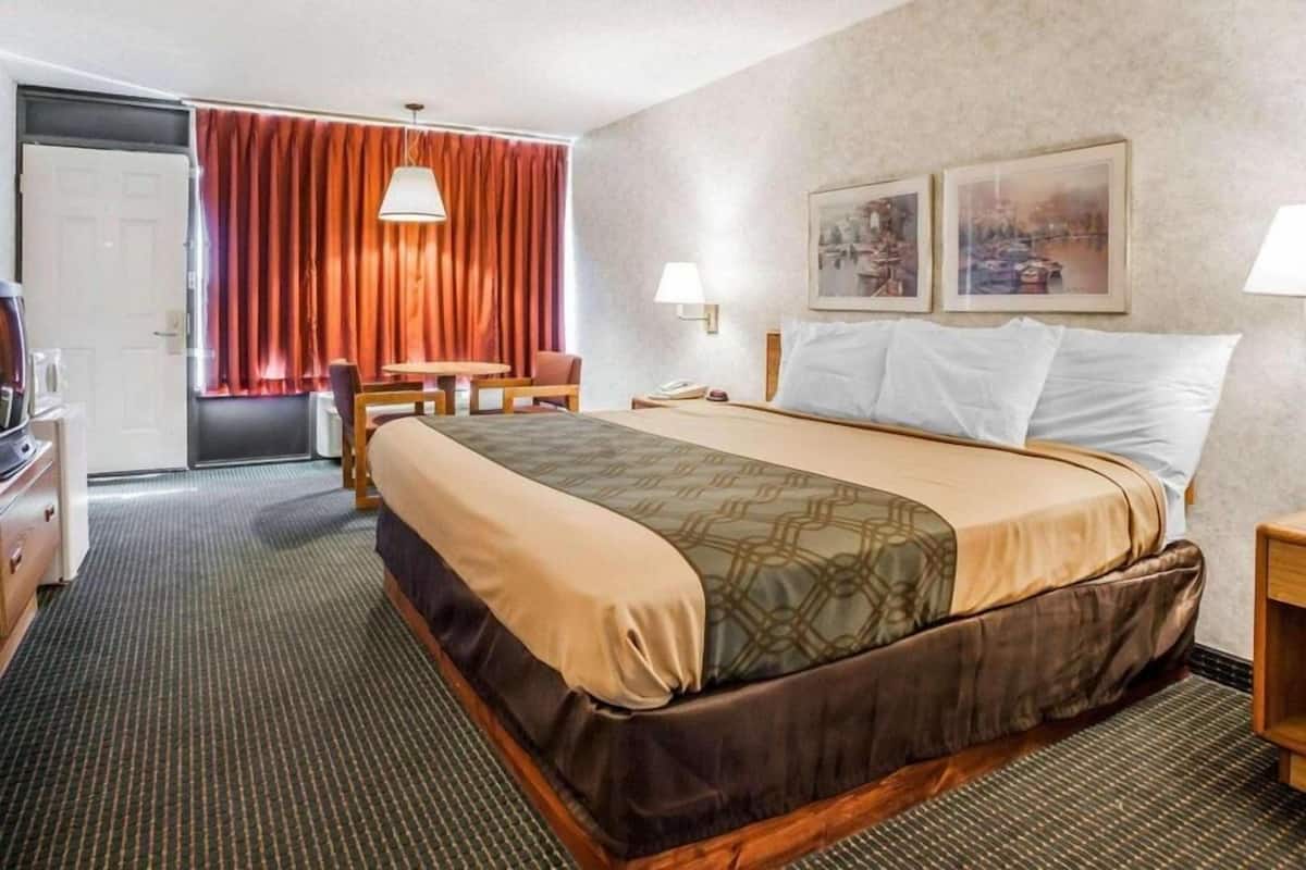 Hotellihuone, jossa on sänky, työpöytä, tuoli, lamppu ja ovi.