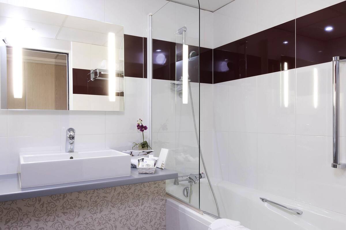 Une salle de bain moderne avec un lavabo blanc, un miroir, une douche et un mur décoré d’un motif.