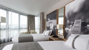 Une chambre d’hôtel avec deux lits, un bureau, une chaise, une lampe et un grand miroir.