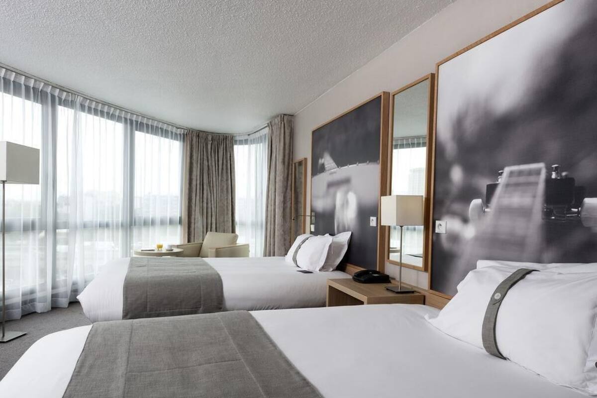 Une chambre d’hôtel avec deux lits, un bureau, une chaise, une lampe et un grand miroir.