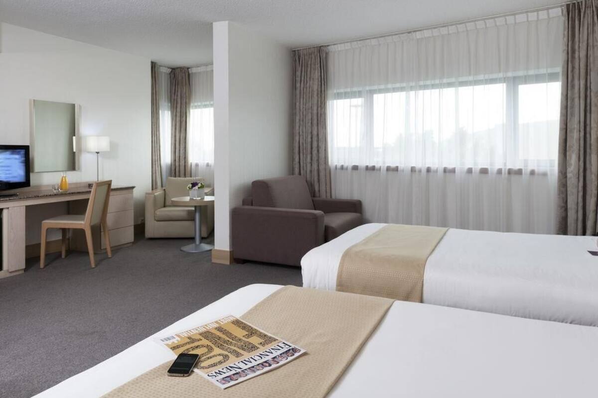 A hotel room with a bed, a desk with a computer, a chair, and a TV.