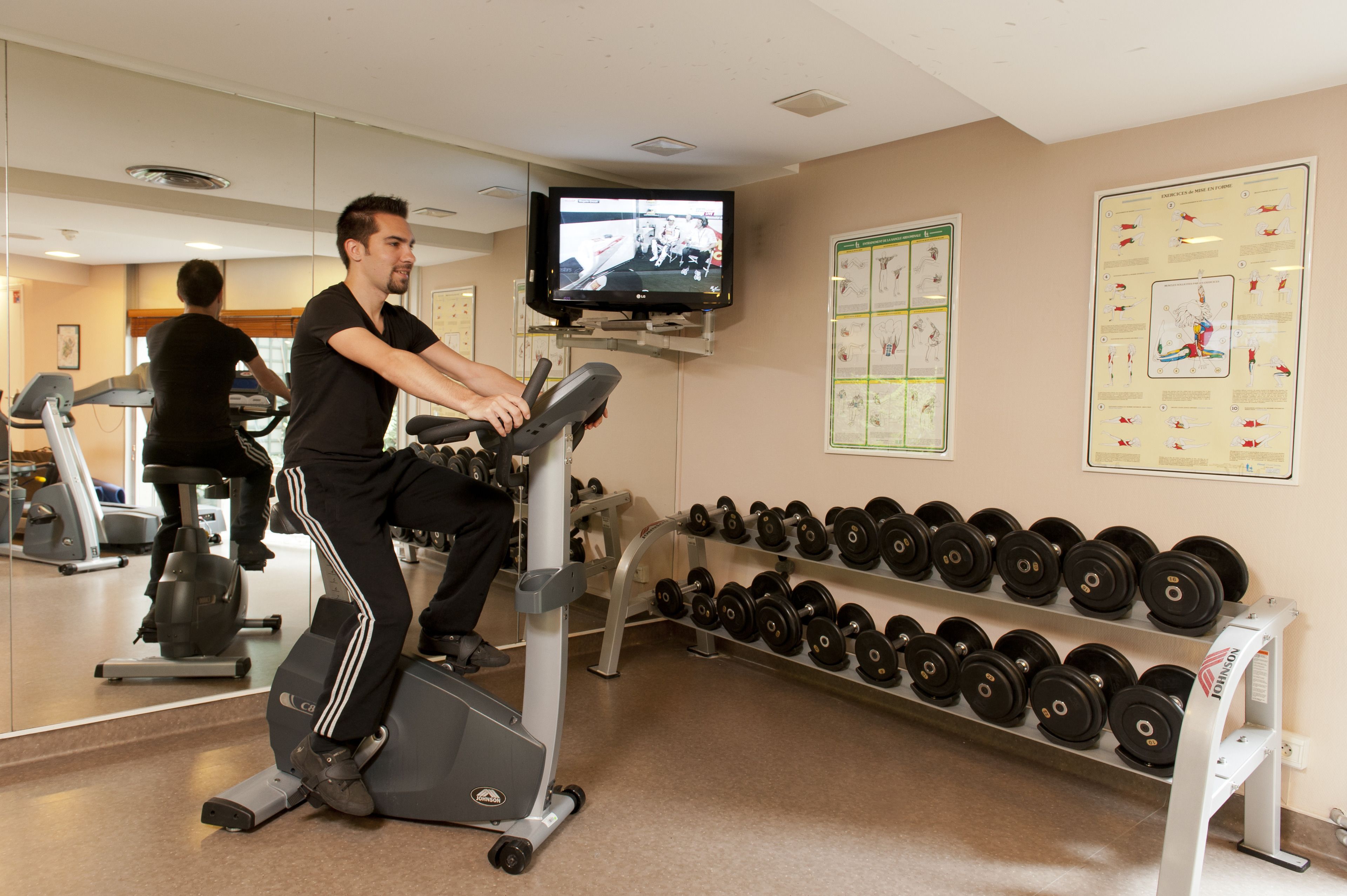 Un gimnasio con equipo de ejercicio, un televisor y carteles informativos en las paredes.