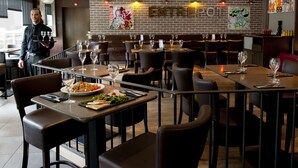 L’intérieur d’un restaurant avec des murs en briques, de nombreuses tables ornées de verres à vin et un serveur en activité.