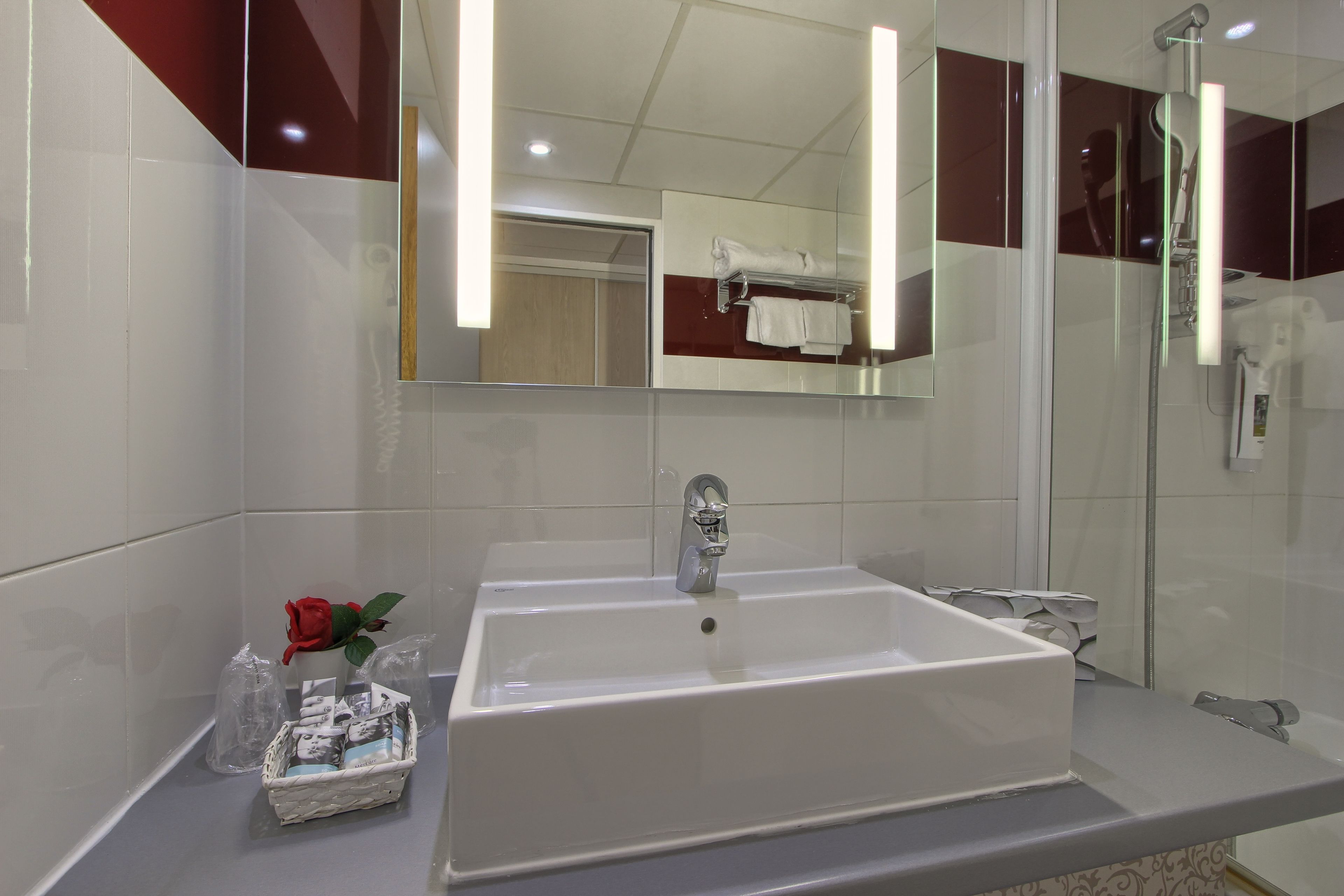 A modern bathroom with a large white sink, a mirror, and a shower.