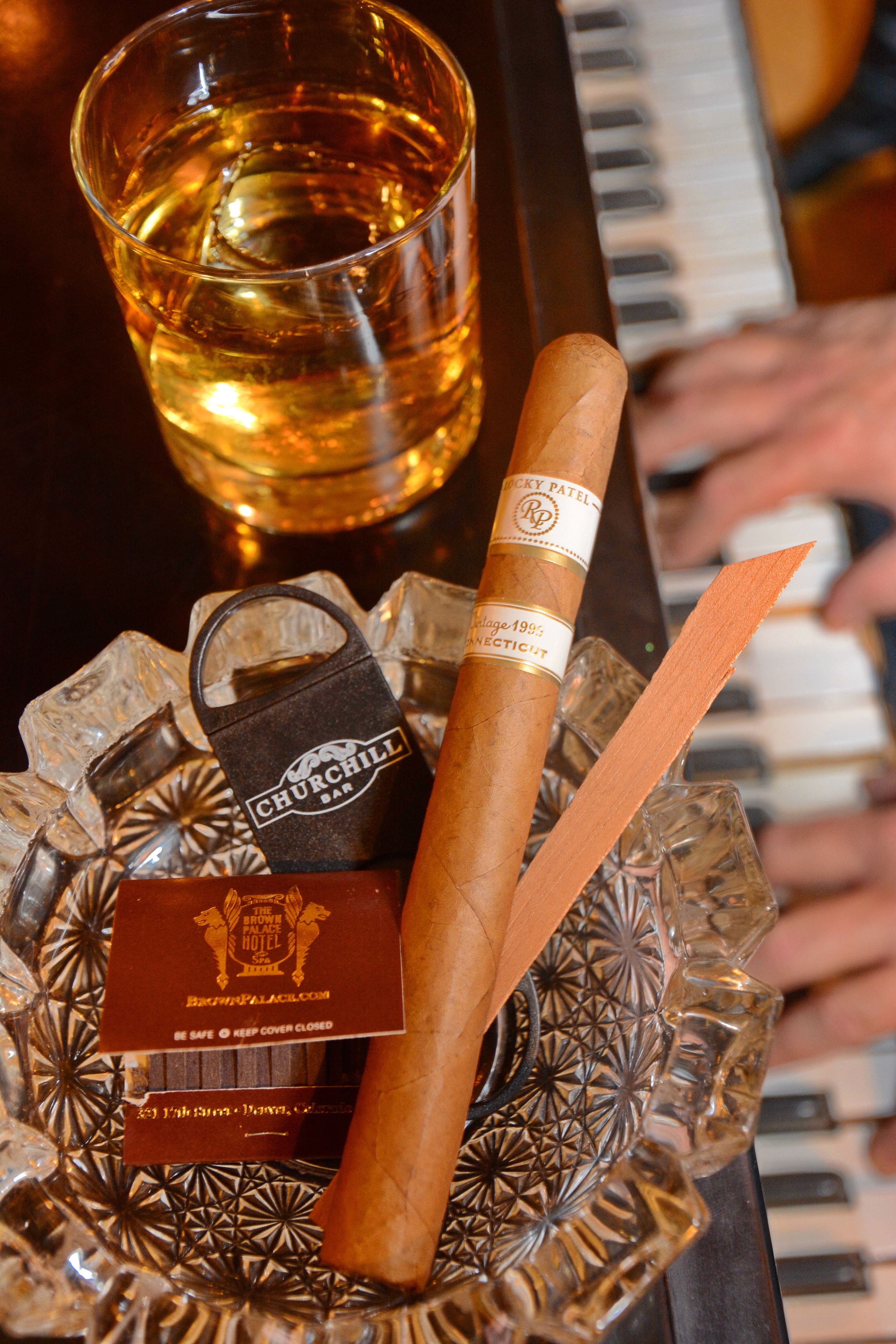 A glass of whiskey, a cigar, and a bar keychain on a decorative tray.