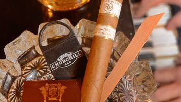 A glass of whiskey, a cigar, and a bar keychain on a decorative tray.