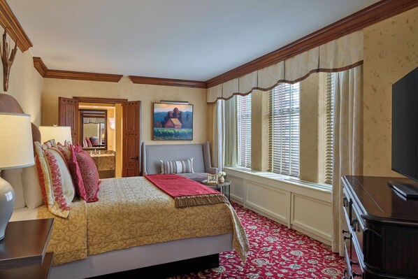 A hotel room with a large bed, a television, a window with blinds, and a painting on the wall.