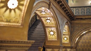 Una amplia escalera con detalles dorados ornamentales y un diseño de pared con motivos.