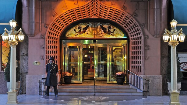 Una entrada imponente con puerta de cristal, guardia de seguridad e iluminación decorativa.