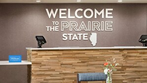 Un comptoir d’accueil orné d’une pancarte « Bienvenue dans l’État de la Prairie », d’une enseigne « Hilton Honors » et d’un mur en bois avec un motif en chevrons.