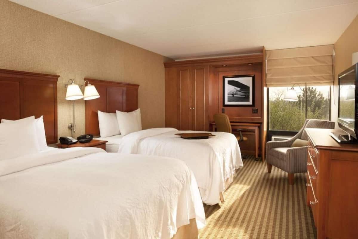 A hotel room with two beds, a desk, a chair, a television, and a window with a view.