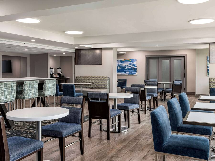 Un vestíbulo de hotel con mesas redondas y sillones tapizados en azul, un mostrador de recepción y un cuadro grande en la pared.