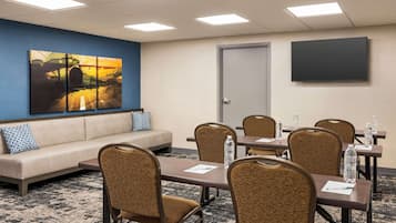 Una sala de conferencias con un sofá, sillas, una mesa, una pantalla de proyector y un cuadro en la pared.