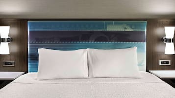 Een hotelkamer met een groot bed, twee witte kussens, een hoofdbord met een blauw-wit gestreept patroon, en twee wandlampen.