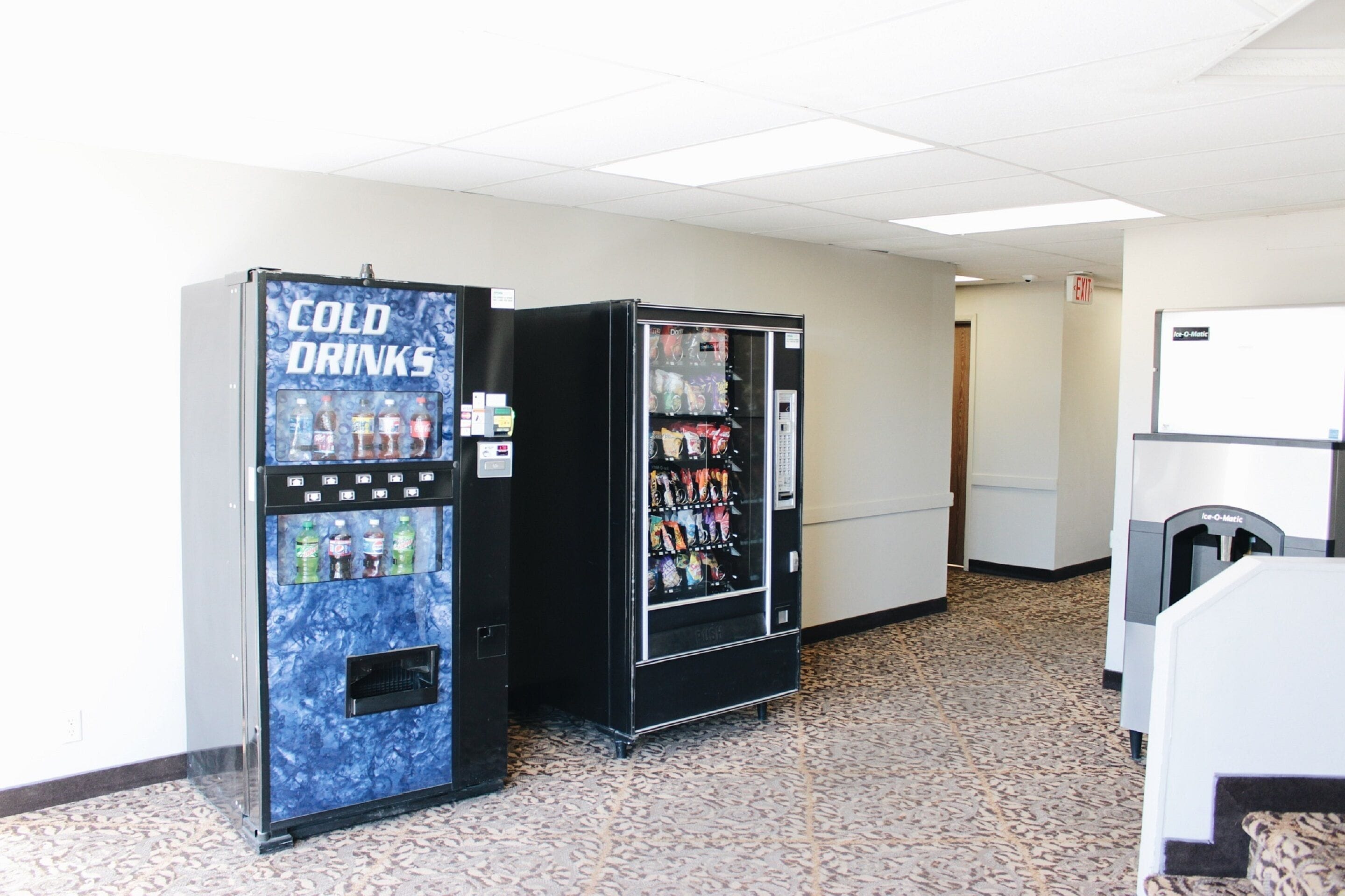 Two vending machines labeled "COLD DRINKS" in a hallway with patterned flooring and a white wall.