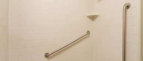 A bathroom with white tiled walls, a handheld showerhead, a grab bar, and a corner shelf.