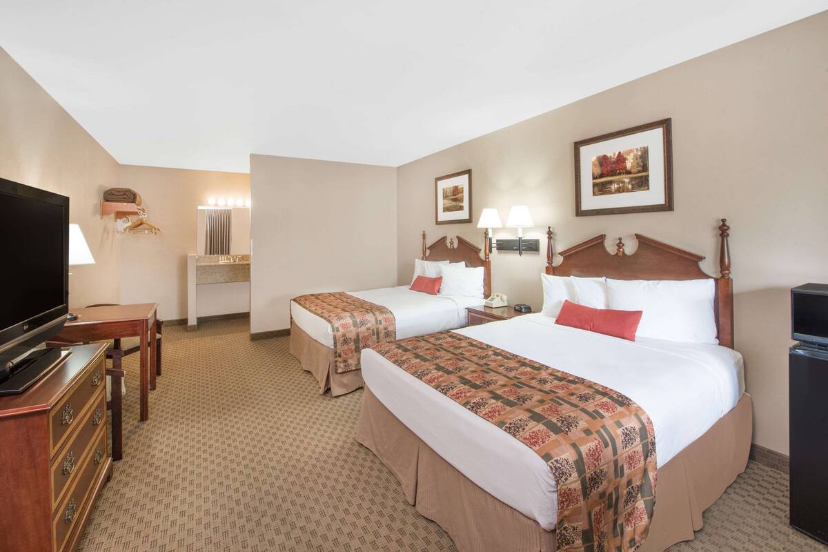 A hotel room with two beds, a TV, a desk, and a dresser.
