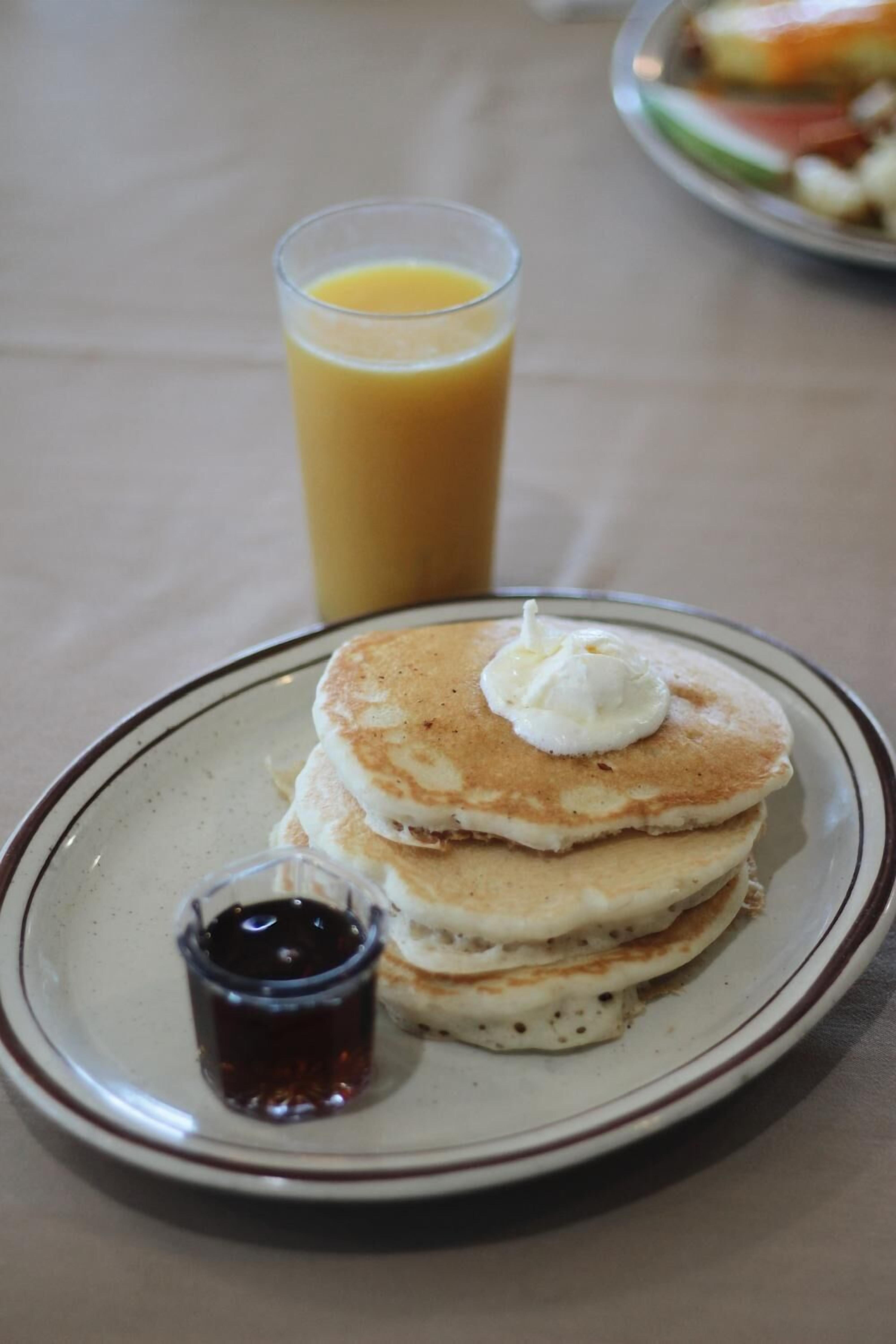 A plate of pancakes with syrup and a glass of orange juice.
