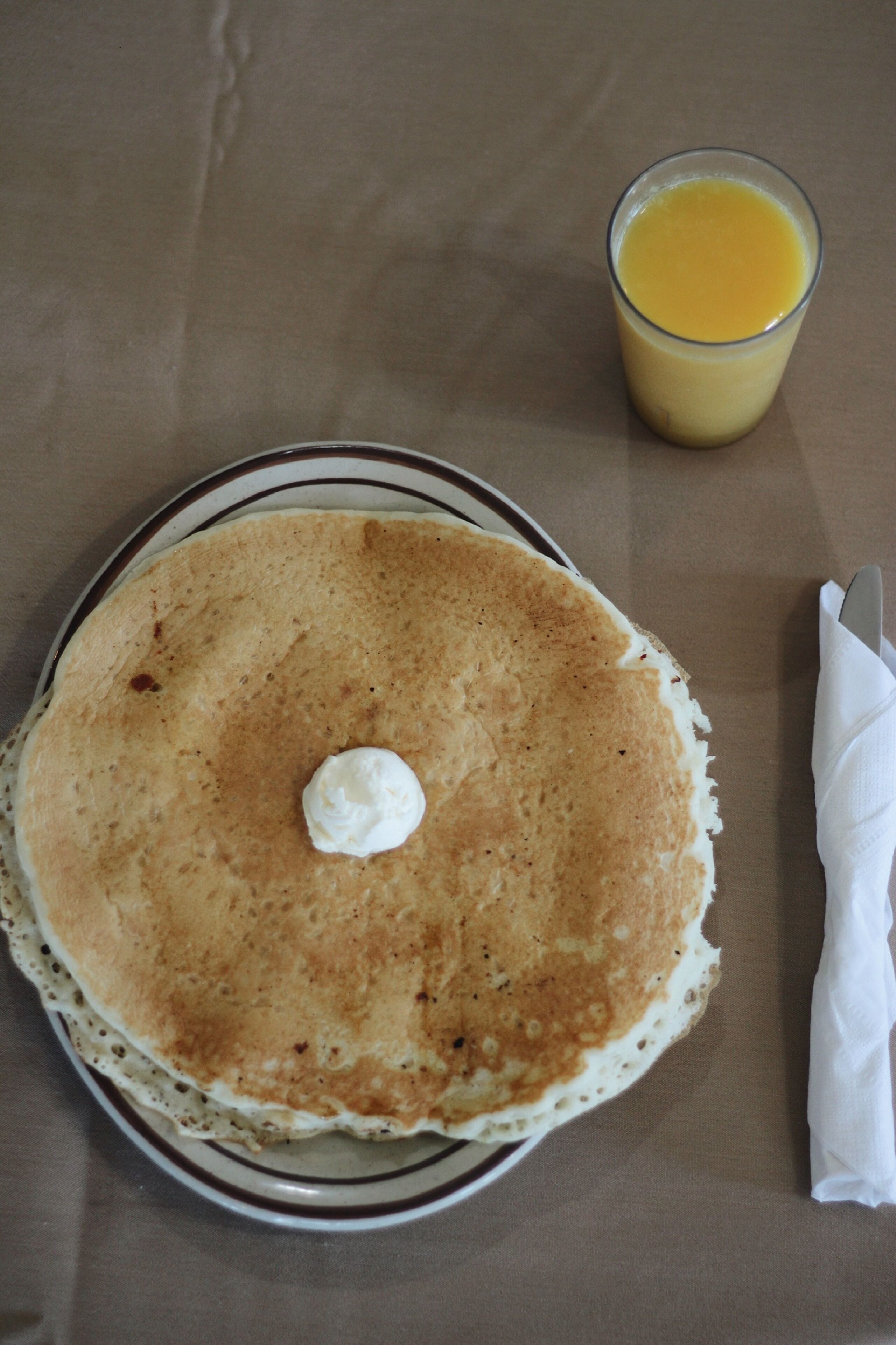 A plate with a pancake and a glass of orange juice on a table.