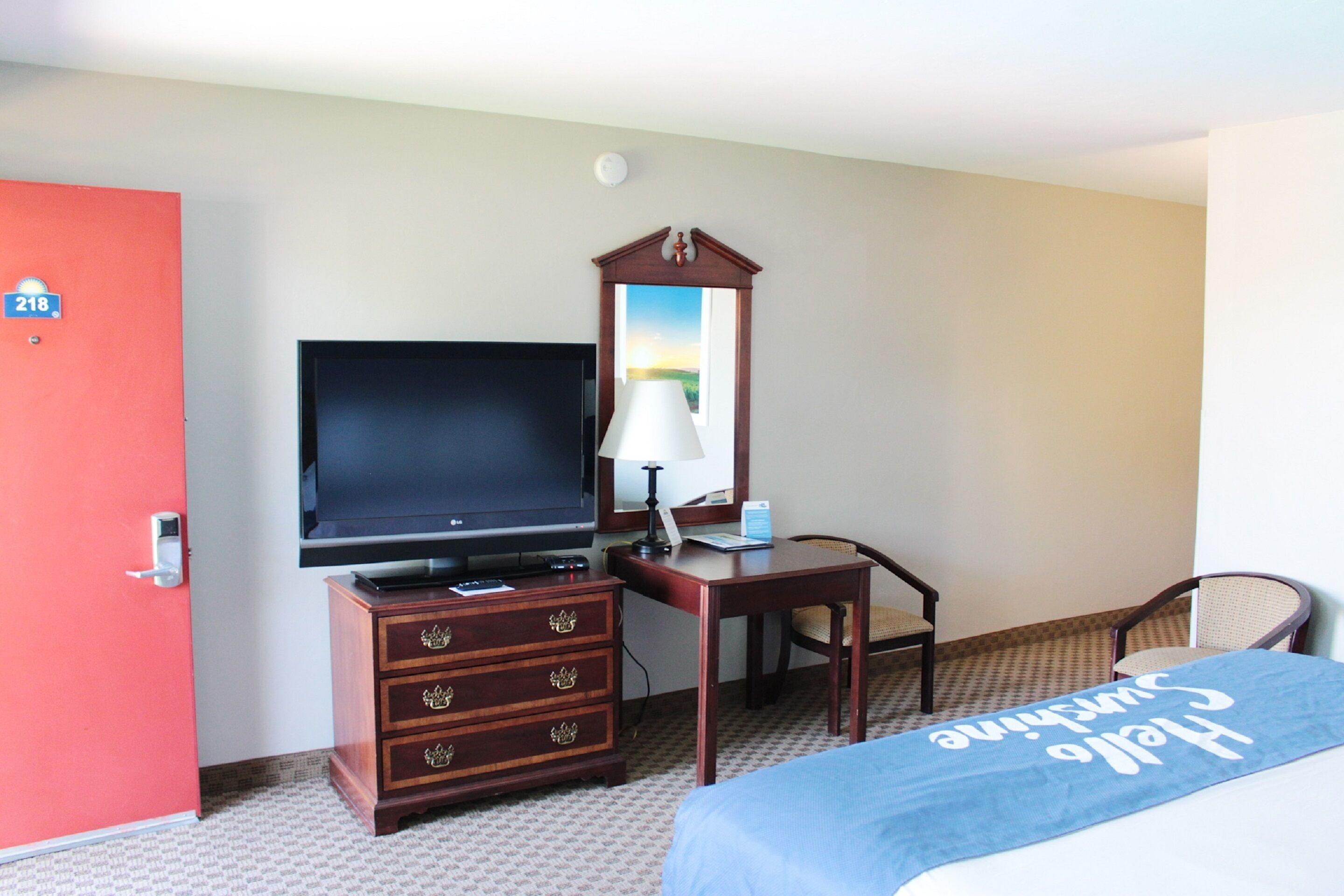 A hotel room with a bed, a desk with a lamp, a television, and a wardrobe.