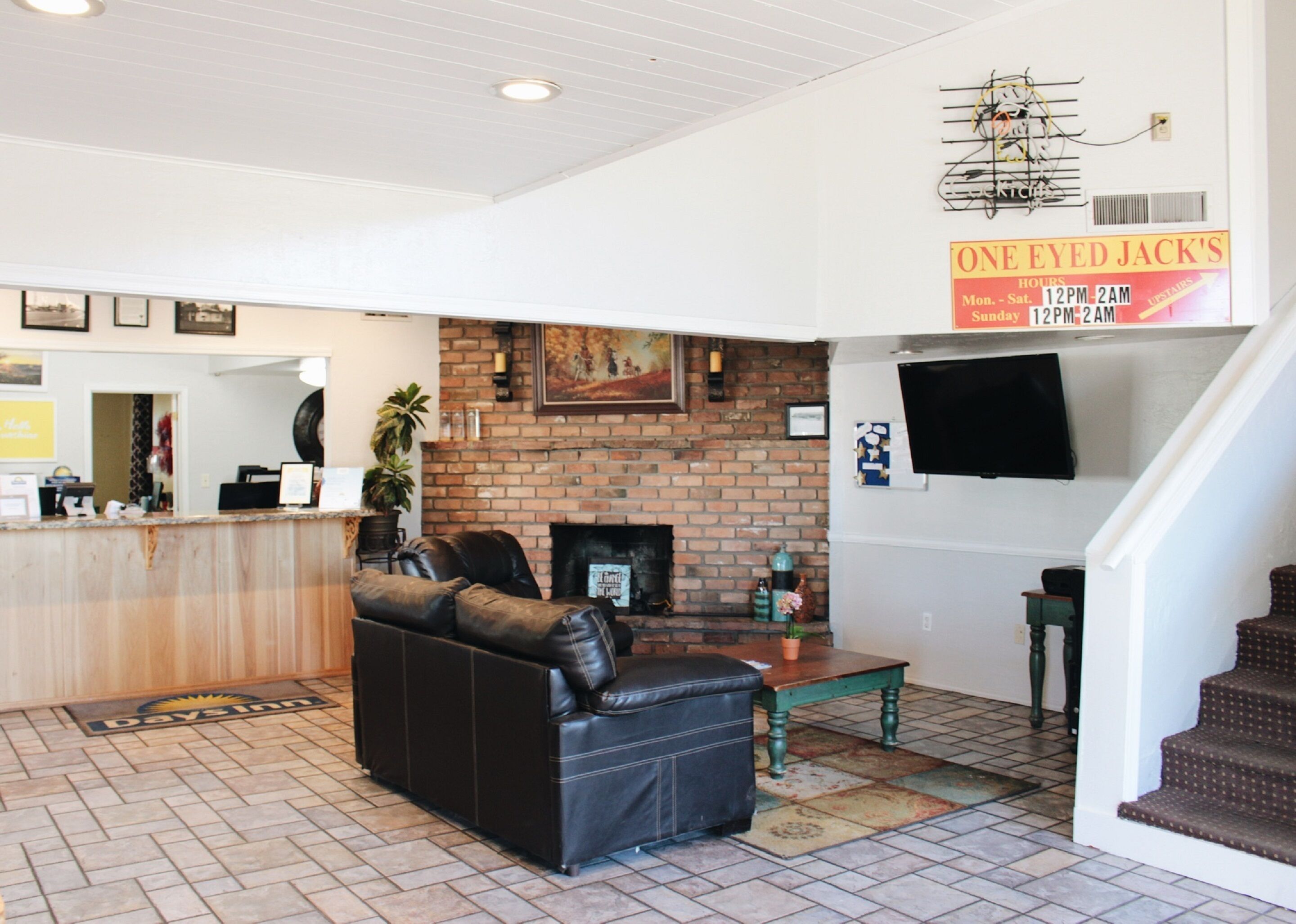 A spacious living area with a leather sofa, a brick fireplace, and a flat-screen TV mounted on the wall.