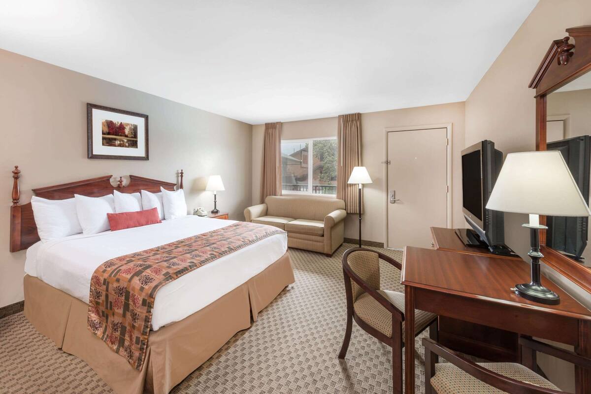 A hotel room with a large bed, a desk, a chair, a television, and a window with curtains.