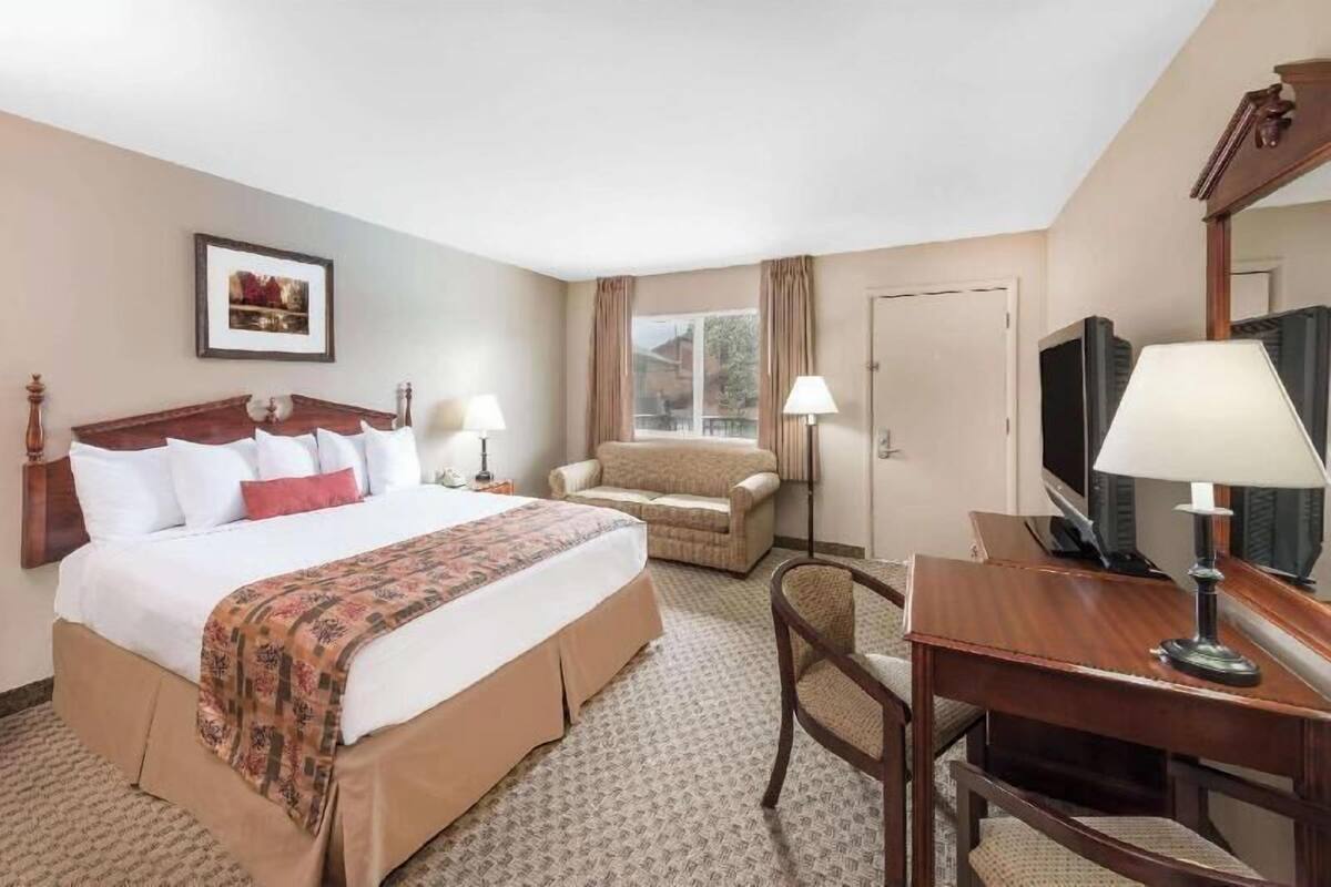 A hotel room with a bed, a sofa, a desk, a television, and a framed picture on the wall.