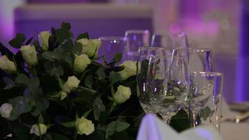 Une table mise avec un arrangement floral composé de roses blanches et de feuilles vertes, accompagné de plusieurs verres à vin transparents.