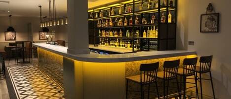 Zona de bar con suelo de cuadros, barra y varios taburetes.