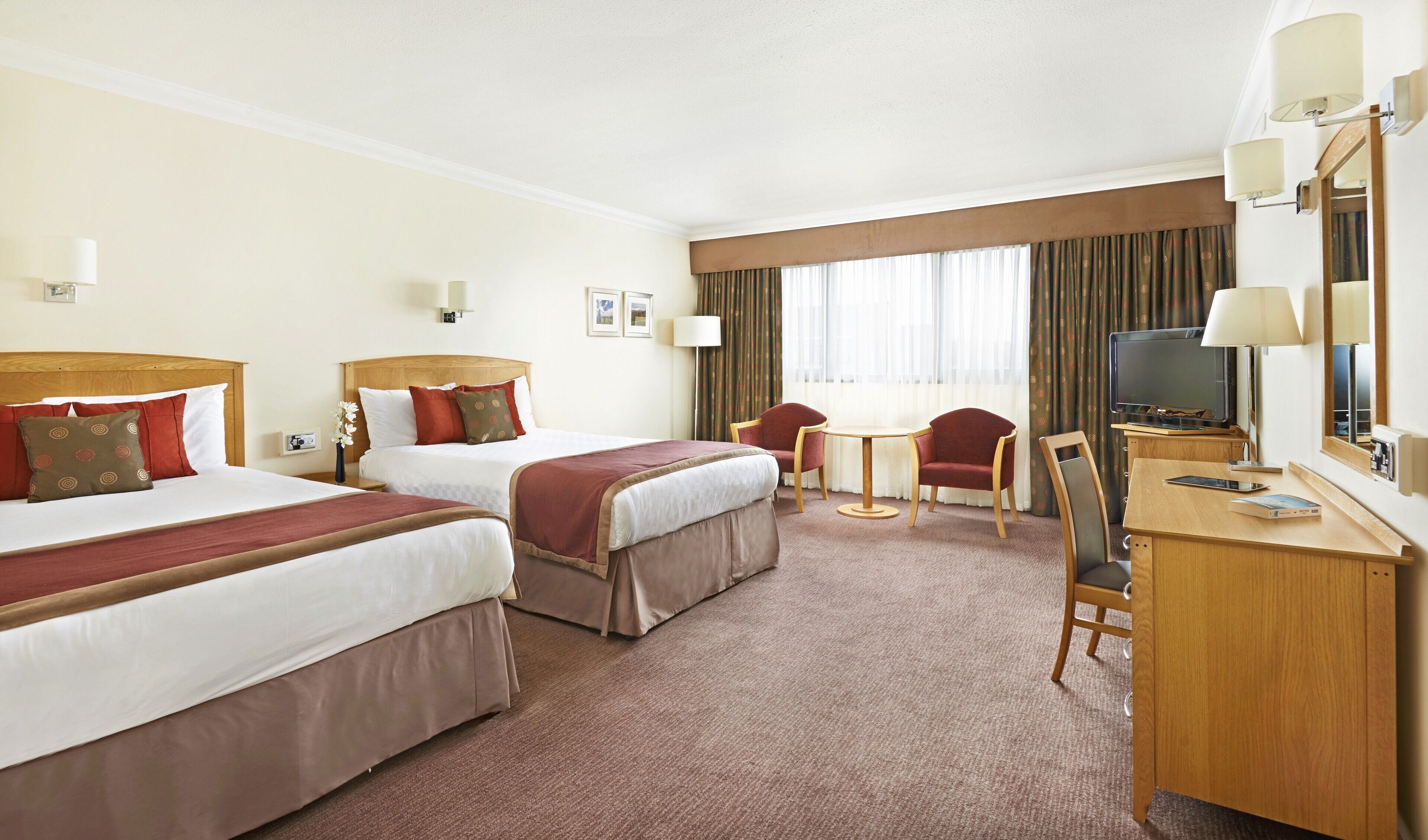 A hotel room with two beds, a desk, a chair, a TV, and a window with curtains.
