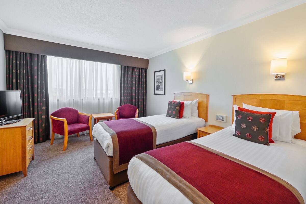 A hotel room with two beds, a TV, a desk, and a chair.