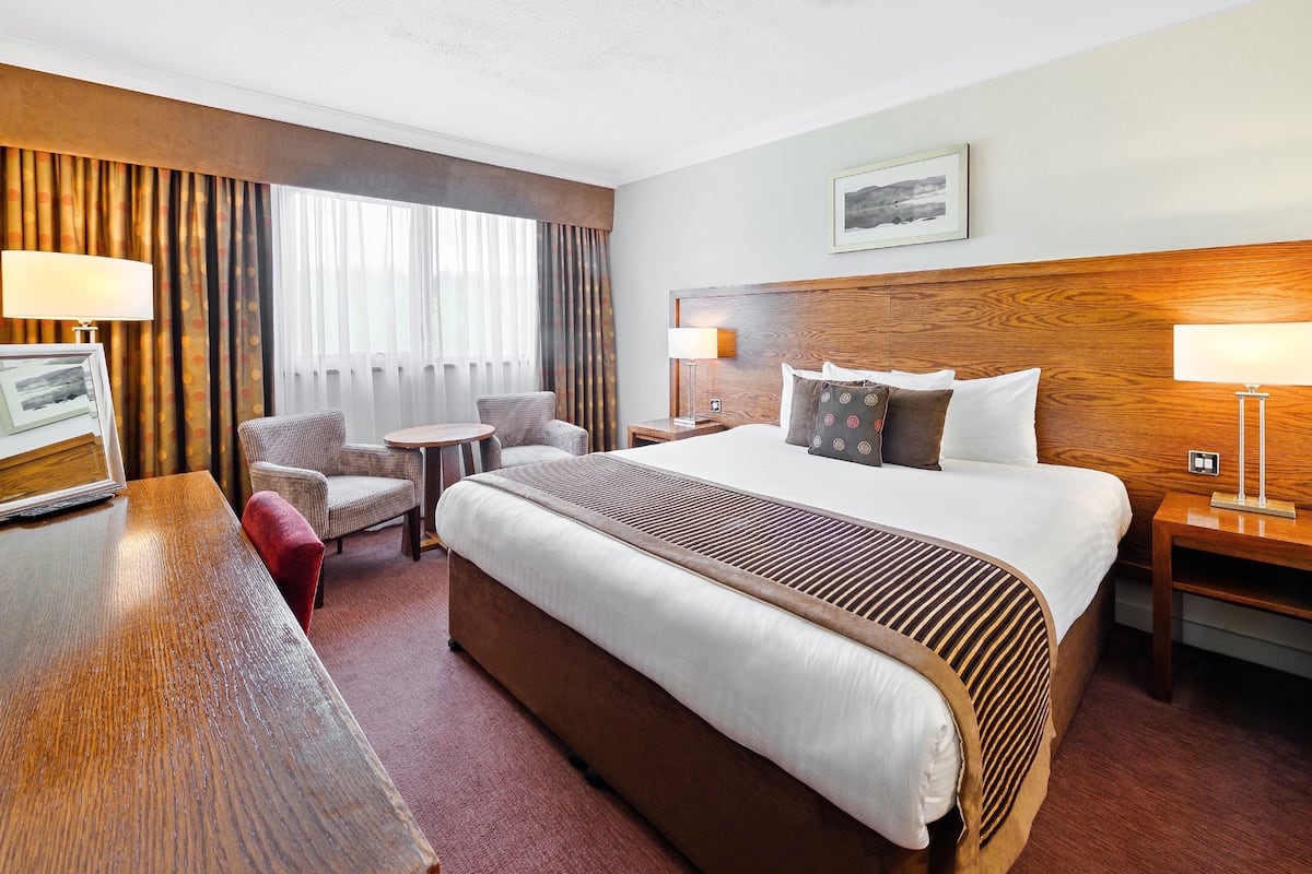 A hotel room with a large bed, a desk, a chair, a small table, and a window with curtains.