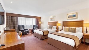 A hotel room with two beds, a desk, a chair, a small table, and a painting on the wall. - The Aberdeen Altens Hotel (Aberdeen)