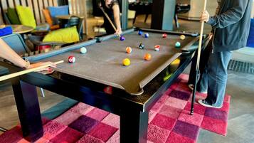 Ein Billardtisch mit Kugeln, eine Person beim Spielen und ein Schachbrettmuster-Teppich.