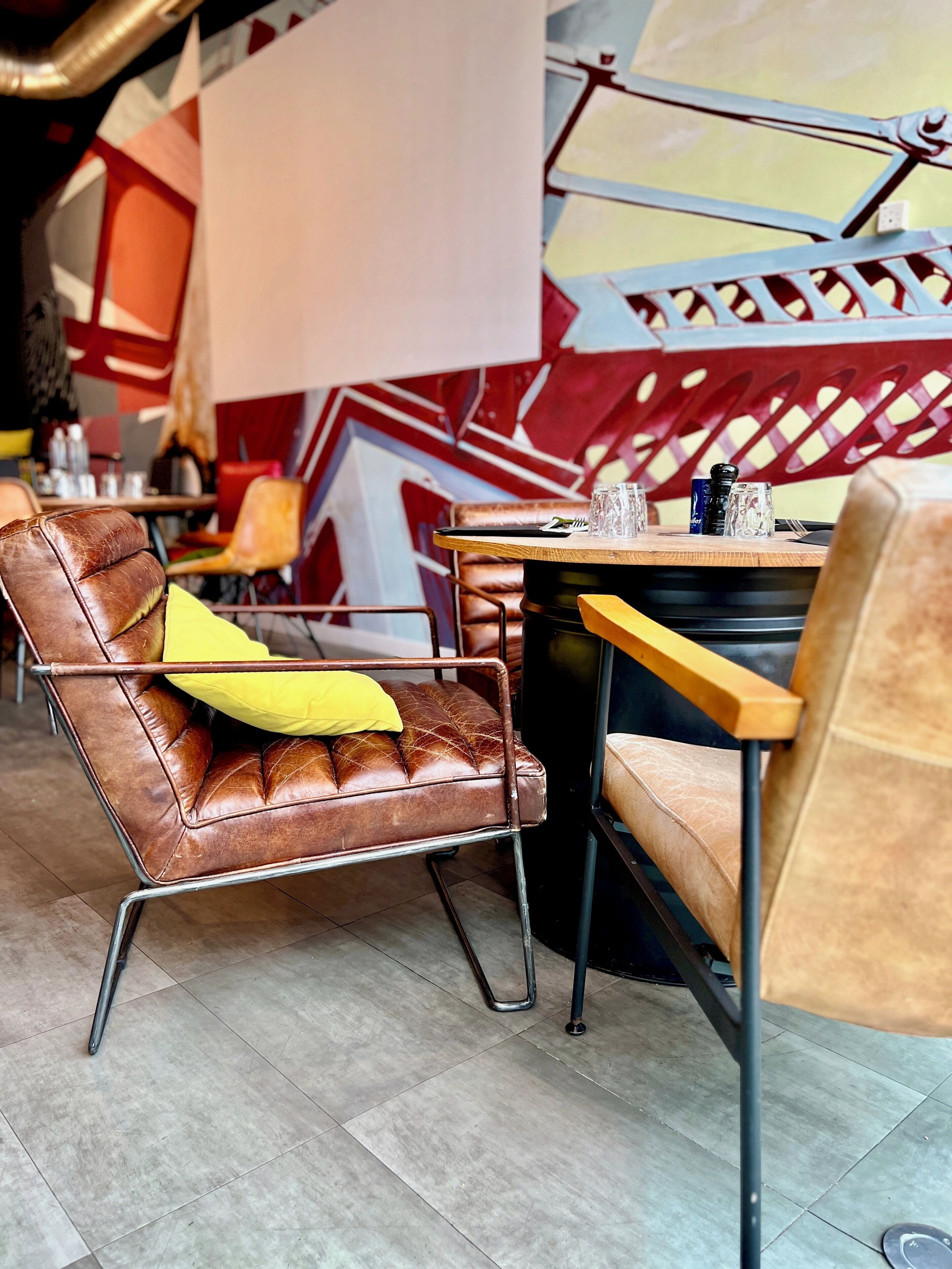 A modern cafe interior with leather chairs, a wooden table, and a geometric wall design.
